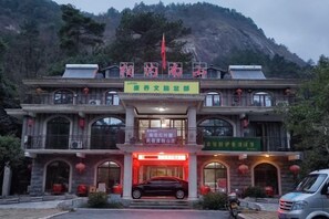 A traditional building with a signboard, multiple windows, and a red car parked in front.