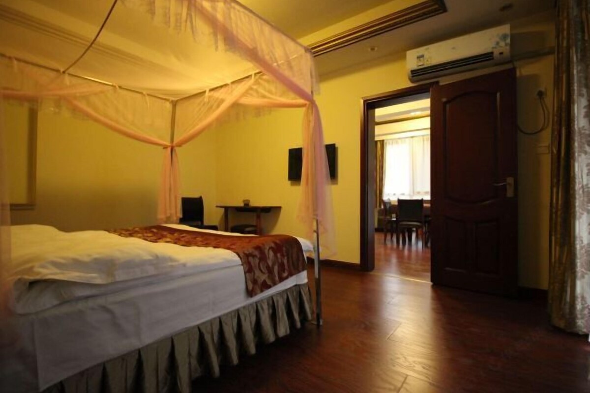 A room with a four-poster bed, a desk, and a door leading to another room.