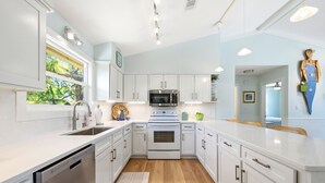 A modern kitchen with white cabinets, stainless steel appliances, and a large window with a view of trees.