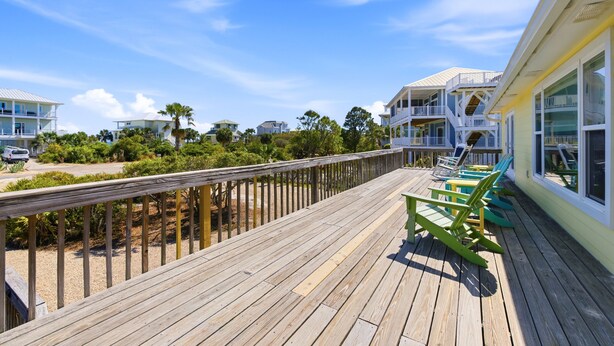 A wooden deck with outdoor seating, a view of beachfront properties, and a clear sky.