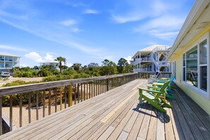 A wooden deck with outdoor seating, a view of beachfront properties, and a clear sky. - Welcome to Key Lime Time! (St. George Island)