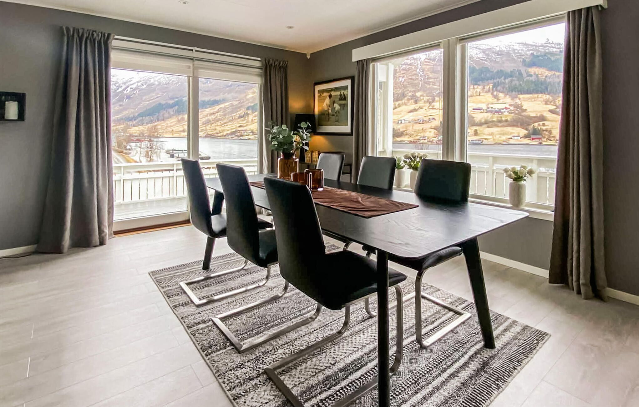 A dining area with a table, chairs, and a view of mountains through large windows.