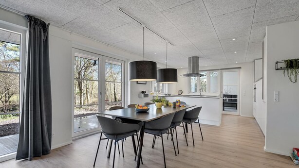 Una cocina moderna con comedor, ventanas amplias y vista a árboles.