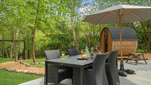 Un patio con una mesa dispuesta para dos, rodeado de sillas de mimbre, un banco de madera y un gran paraguas.