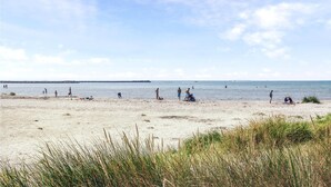 Una playa con gente y barcos a lo lejos.