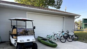 A white golf cart parked in front of a garage, with a green kayak and two bicycles leaning against the garage door. - Sandy Toes · New renovated Sandy Toes!!! (Port Saint Joe)