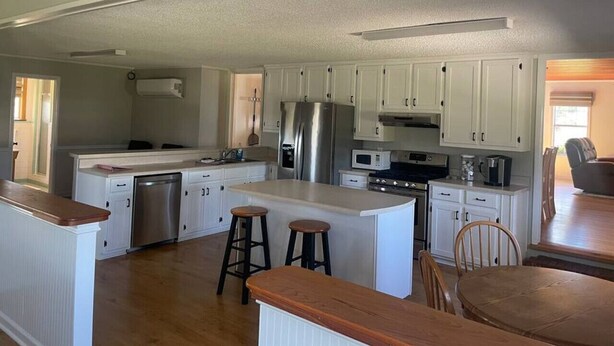 A spacious kitchen with white cabinetry, a central island with stools, stainless steel appliances, and a dining area with a wooden table and chairs. - Sandy Toes · New renovated Sandy Toes!!! (Port Saint Joe)