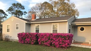 A single-story house with a light gray exterior, a chimney, and a well-maintained front yard with pink flowering bushes. - Sandy Toes · New renovated Sandy Toes!!! (Port Saint Joe)