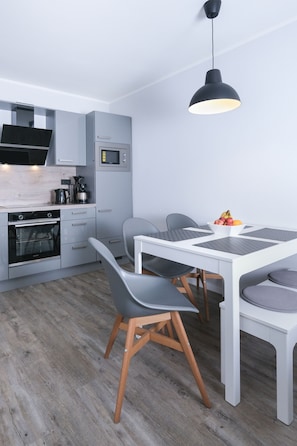 A modern kitchen with grey cabinets, a white countertop, a built-in oven, a microwave, and a hanging pendant light.