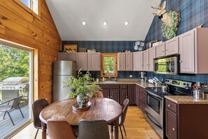 A modern kitchen with wooden cabinetry, stainless steel appliances, and a dining area with a wooden table and chairs.