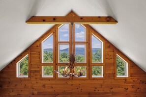 A room with a sloped ceiling and large windows offering a view of a forested landscape. - Peaceful Mountain Getaway: hiking, hot tub, and views (Wardensville)