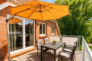 A patio with a table and chairs, an umbrella, and a brick house.