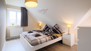 Un dormitorio moderno con una cama blanca, ropa de cama escocesa y dos lámparas de noche.