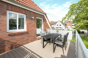A balcony with a table and chairs, a brick wall, and a window.