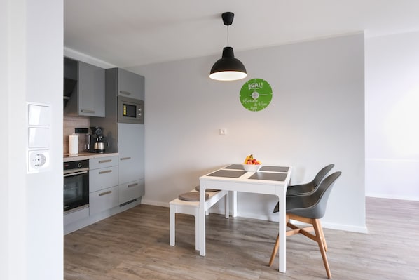 A modern kitchen with grey cabinets, a white dining table, and a black pendant light.