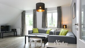 Una sala de estar moderna con un sofá gris, una mesita de centro blanca y un televisor sobre un mueble.