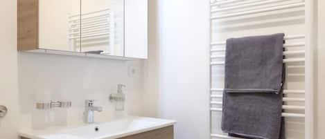 Un baño con tocador de madera, un espejo con luces, un perchero para toallas y un radiador blanco.