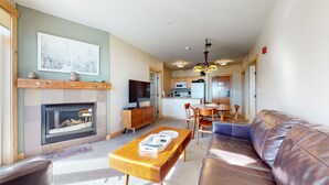 Una sala de estar con chimenea, televisor, una mesa de centro de madera, un sofá de cuero y una zona de comedor con mesa y sillas.
