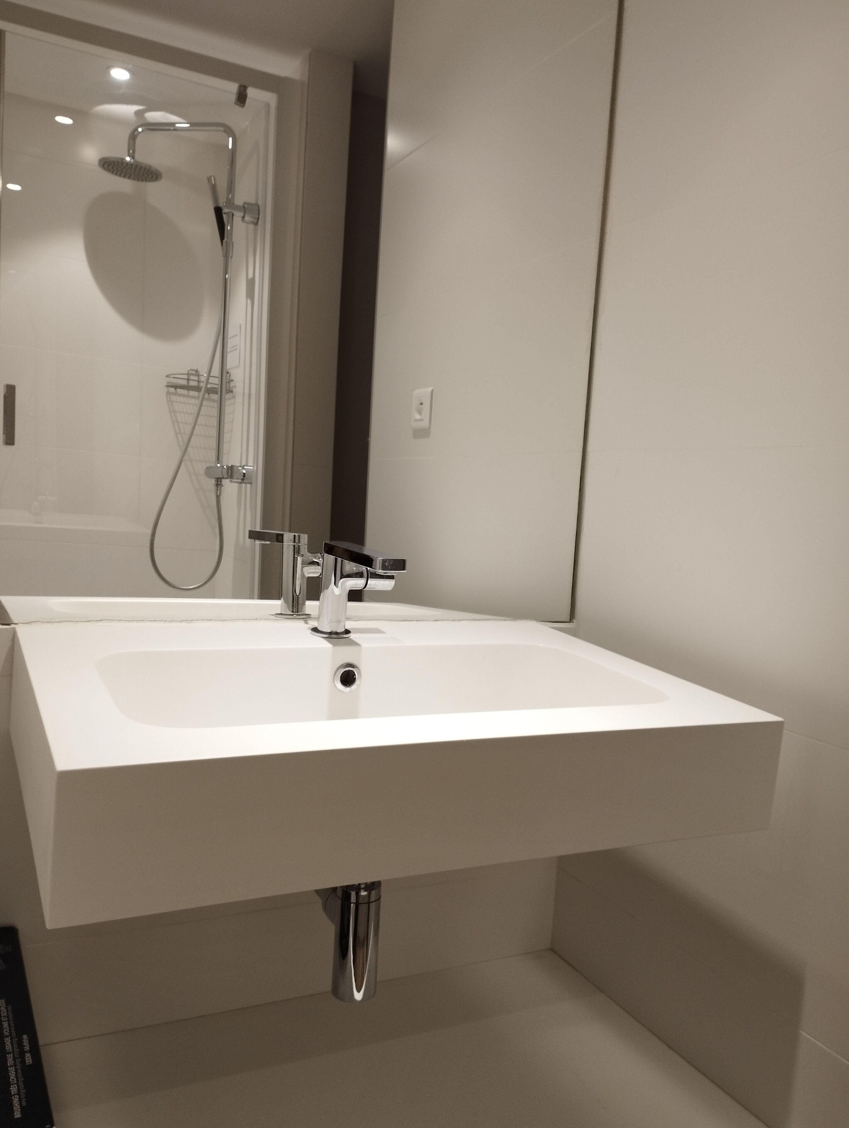 Un baño moderno con un lavamanos blanco grande, un cabezal de ducha y un perchero para toallas.