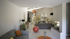 Una sala de estar moderna con un sofá gris, una mesa de centro redonda naranja y una pelota roja de ejercicio.