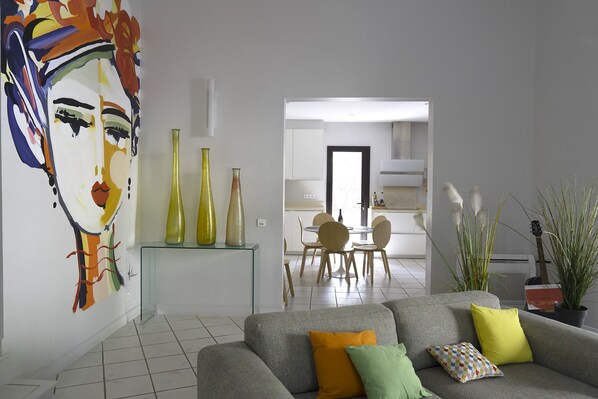 Un salon moderne avec un canapé gris, des coussins colorés, une table basse en verre et une peinture abstraite aux couleurs vives accrochée au mur.