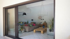 Una sala de estar moderna con un gran ventanal corredero, un conjunto de sofás, una mesa de centro y varias plantas.