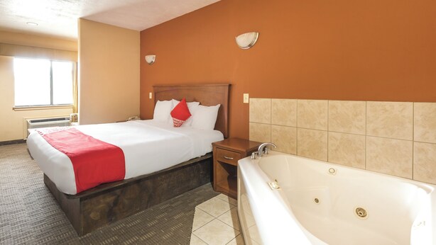 Quarto de hotel com cama, mesa de cabeceira, banheiro com banheira e janela com cortinas.