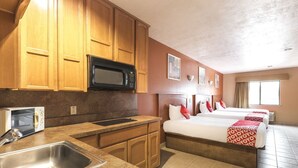 Quarto de hotel com cozinha compacta, cama com roupa de cama vermelha e branca, e uma janela grande.