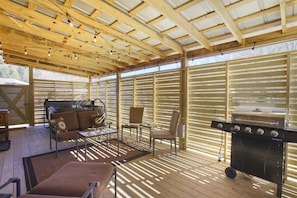 An outdoor patio with a wooden deck, a barbecue grill, and a seating area with a sofa and chairs.