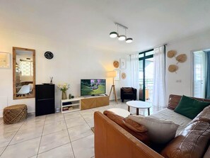 A modern living room with a sofa, TV, and a dining area with chairs.