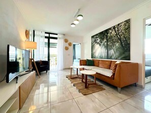A modern living room with a flat-screen TV, a sofa, a coffee table, and a large painting of trees.