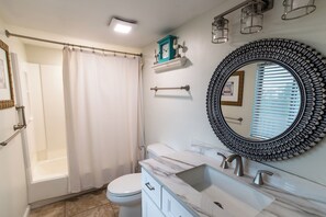 Une salle de bain équipée d’une baignoire, de toilettes, d’un meuble-lavabo et d’un grand miroir.