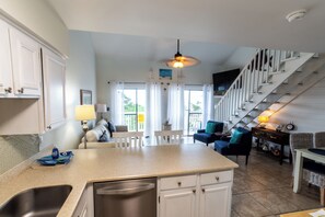 A kitchen with a central island, a dining area with chairs, a staircase, and a living room with a sofa. - Cute & Cozy Steps the Beach (SANTA ROSA BEACH)