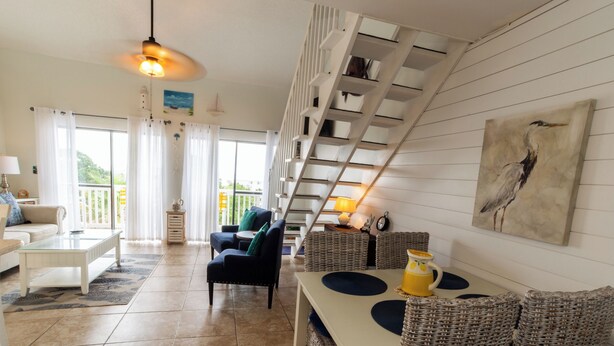 Un vaste espace de vie comprenant un canapé, des fauteuils, une table basse, une table à manger, un escalier et un balcon.