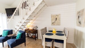 Un escalier menant à une mezzanine, un coin repas avec une table et des chaises, et des œuvres d’art accrochées aux murs.