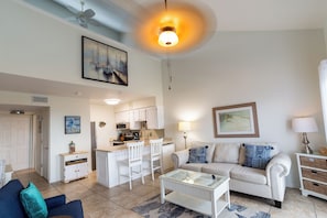 A living room with a sofa, coffee table, and a dining area with chairs and a kitchen. - Cute & Cozy Steps the Beach (SANTA ROSA BEACH)
