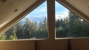 A room with a sloped ceiling and two large windows offering a view of a forest and mountains. - Ashford cabin,Mt. Rainier view. Private river access, 17 acres, 5 mi to MRNP (Ashford)