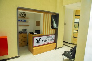 A reception desk with a sign for Victory Villa Apartment Hotel, wooden cabinets, a clock, and a chair. - Victory Villa Apartment Hotel (Kigali)