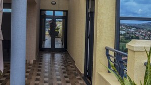 Ein Korridor mit Schachbrettfußboden, einer Glastür zum Außenbereich und Blick auf die Stadt durch ein Fenster.