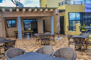 An outdoor patio with tables and chairs, a pool table, and a view of a mountainous landscape. - Victory Villa Apartment Hotel (Kigali)