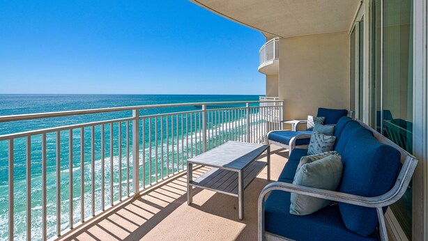 Ein Balkon mit Blick auf das Meer, eine Couch mit Kissen und ein kleiner Tisch.