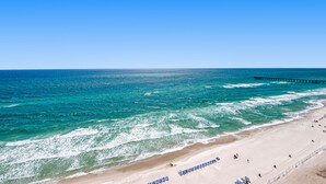 Ein Strand mit klarem, blauem Wasser, einem Steg und Reihen blauer Liegen.