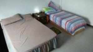 Quarto pequeno com uma cama de solteiro, parede simples, mesa de cabeceira e colcha colorida listrada.