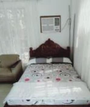 A bedroom with a single bed, a chair, and a wall-mounted air conditioning unit.