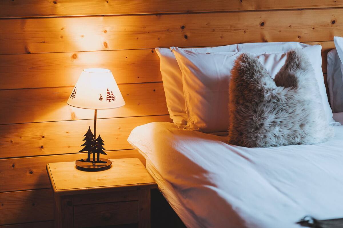 A wooden cabin room with a bed, a nightstand with a lamp, and a fluffy pillow.