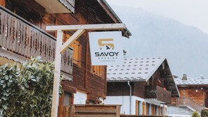Un edificio de madera con un letrero que dice 'SAVOY MORZINE' y una montaña nevada al fondo.