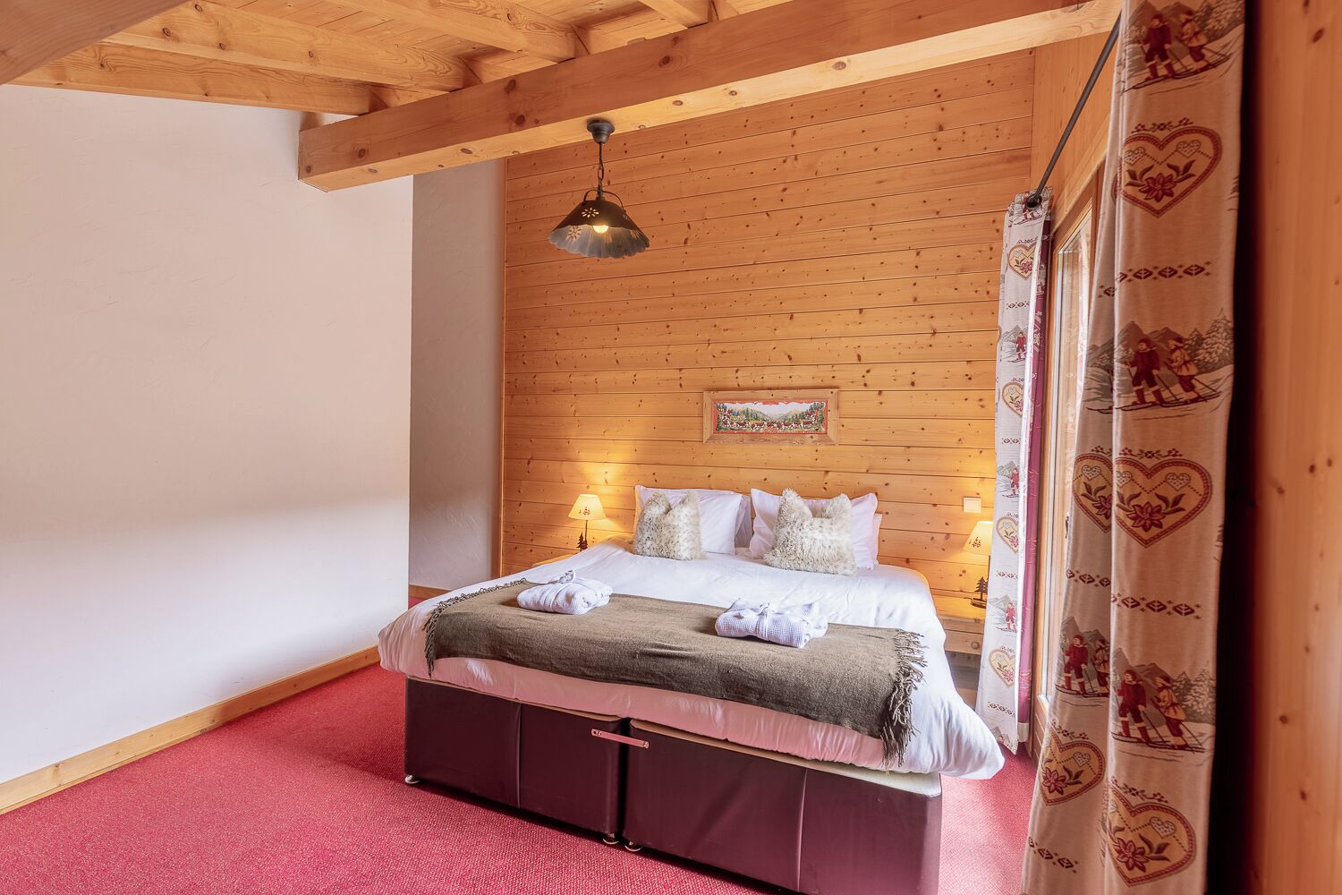 Une chambre avec un plafond en bois, un lit avec une literie blanche, une tête de lit ornée d’un tableau et un tapis rouge.
