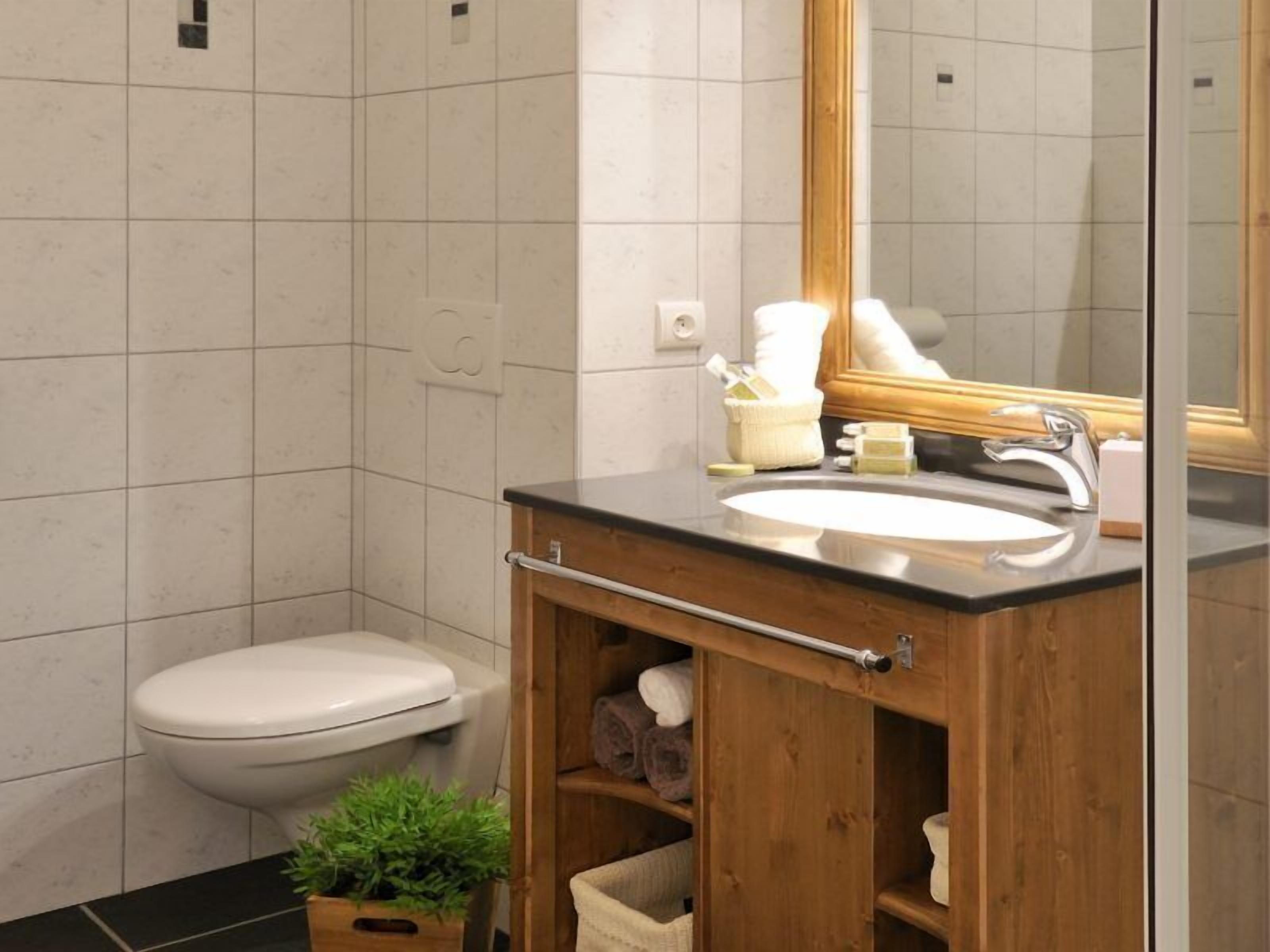 A modern bathroom with a wooden vanity, white toilet, and a mirror above the sink.