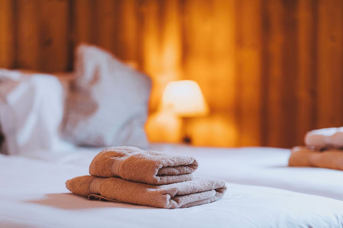 A neatly made bed with folded towels and a lamp in the background.