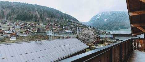 A balcony with a view of a village, wooden houses, and snow-covered mountains.